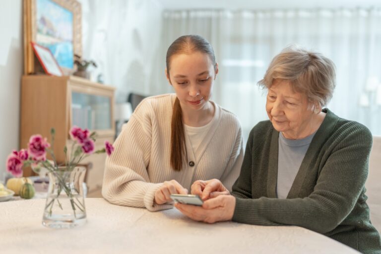 Young,Woman,Helping,An,Senior,Woman,With,A,Smartphone,At