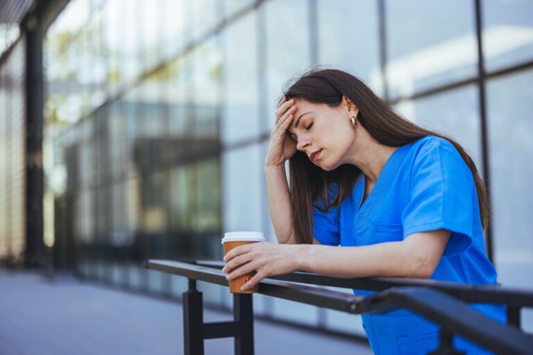 A,Tired,Healthcare,Worker,In,Blue,Scrubs,Leans,On,A
